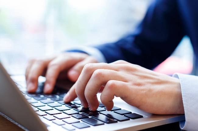 Hands of young businessman pressing keys of laptop